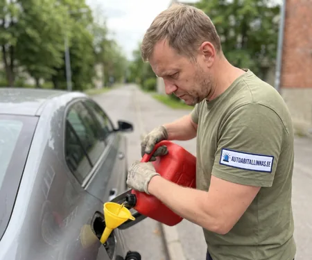 Technician pouring fuel into a grey car through a yellow funnel; an absorbent mat catches drips.