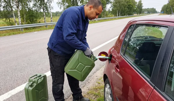 Technician pouring fuel from a green can into a red car beside a main road; we delivered fuel to 296 cars in 2025.