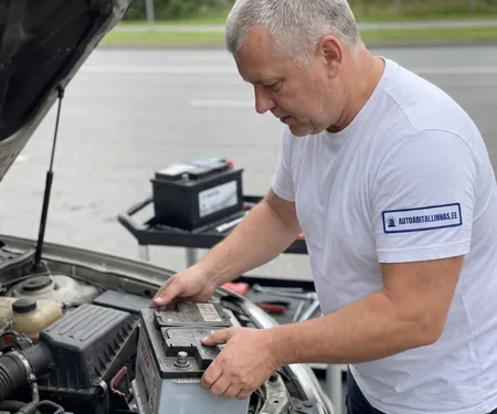 Tehnik vahetab tee ääres auto akut, taga tööriistakärul teine aku, pärast akuvahetust seatakse kliendi juuresolekul õigeks kell ja aknatõstukite automaatika.