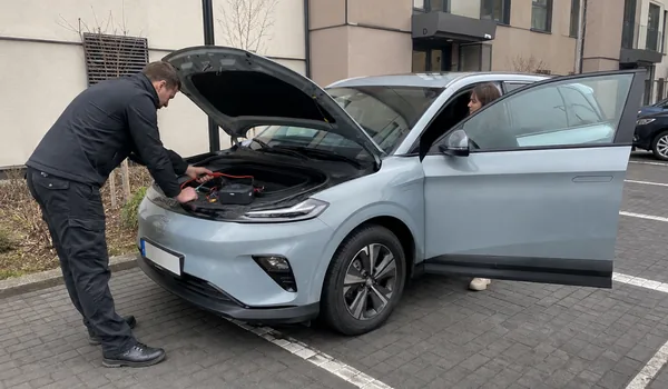 Hübriid- ja elektriauto käivitusabi, tehnik töötab helesinise elektriauto avatud kapoti all, juhiistmel istuv klient vajutab käivitusnuppu tehniku märguandel.