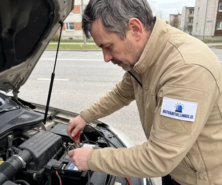 Tehnik kinnitab kortermajade vahelisel tänaval punase klambri aku plussklemmile, külma ilmaga ootab klient käivituse ajal soojas kaubikus.