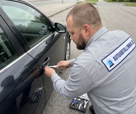 Tehnik avab tumeda sõiduauto juhiust lukuavamistööriistaga, maas tööriistakohver, haakeriista konksu painutab iga tehnik endale ise.